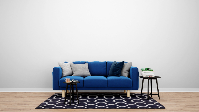 Un canapé bleu, des coussins, deux tables noires, un tapis à motifs et un mur blanc.