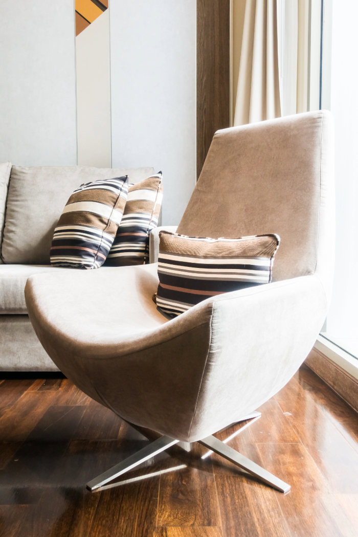 Fauteuil beige avec coussins rayés, recouvert d'une housse, accompagné d'un canapé sur un sol en bois chaleureux.