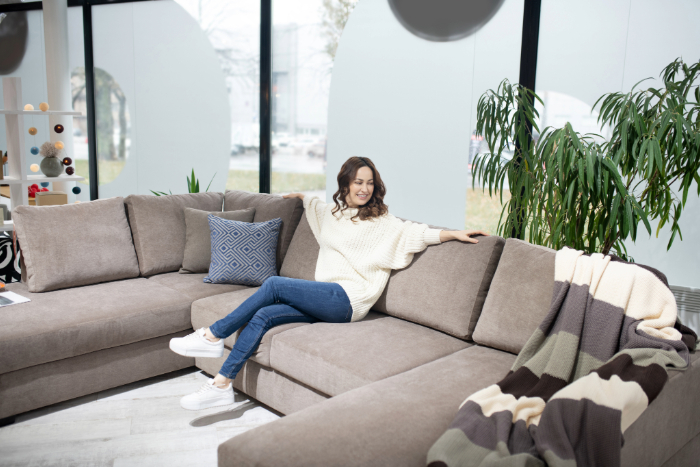 Femme assise sur un canapé beige confortable, entourée de plantes et lumière naturelle.
