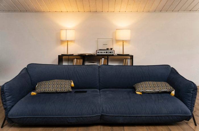 Canapé bleu foncé moderne, deux coussins décoratifs, lampe douce, meuble noir avec livres et appareil vintage.