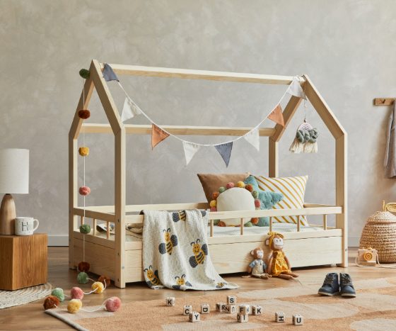 chambre de bébé style jungle avec lit, coussins, peluches, guirlande, jouets, tiroirs, tapis, étagère et paniers.