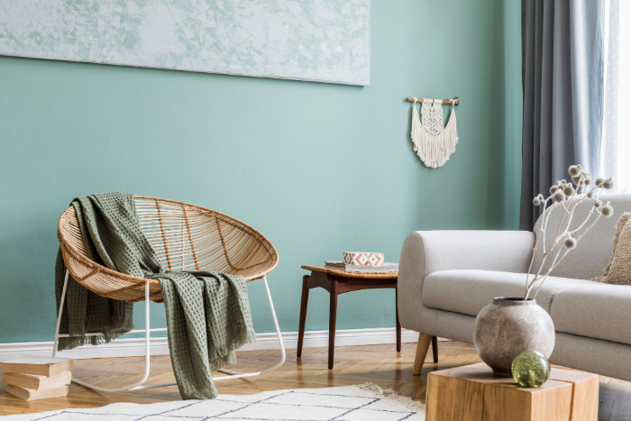 espace cosy incluant canapé gris clair, plaid vert, chaise en rotin, décoration murale bohème avec un mur peint en vert sauge, une teinte apaisante pour décorer une maison neuve.