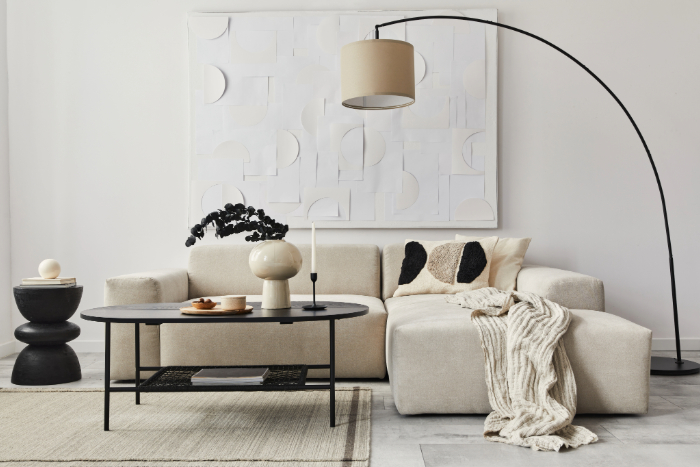 Intérieur maison simple avec canapé, table basse, tapis et lampe arc : décoration minimaliste et couleurs neutres.