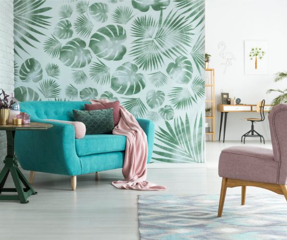 Déco bien-être d'un salon moderne avec mur à motifs feuilles tropicales, plantes, canapé turquoise, fauteuil rose, table ronde et tapis.