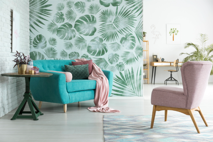Déco bien-être d'un salon moderne avec mur à motifs feuilles tropicales, plantes, canapé turquoise, fauteuil rose, table ronde et tapis.