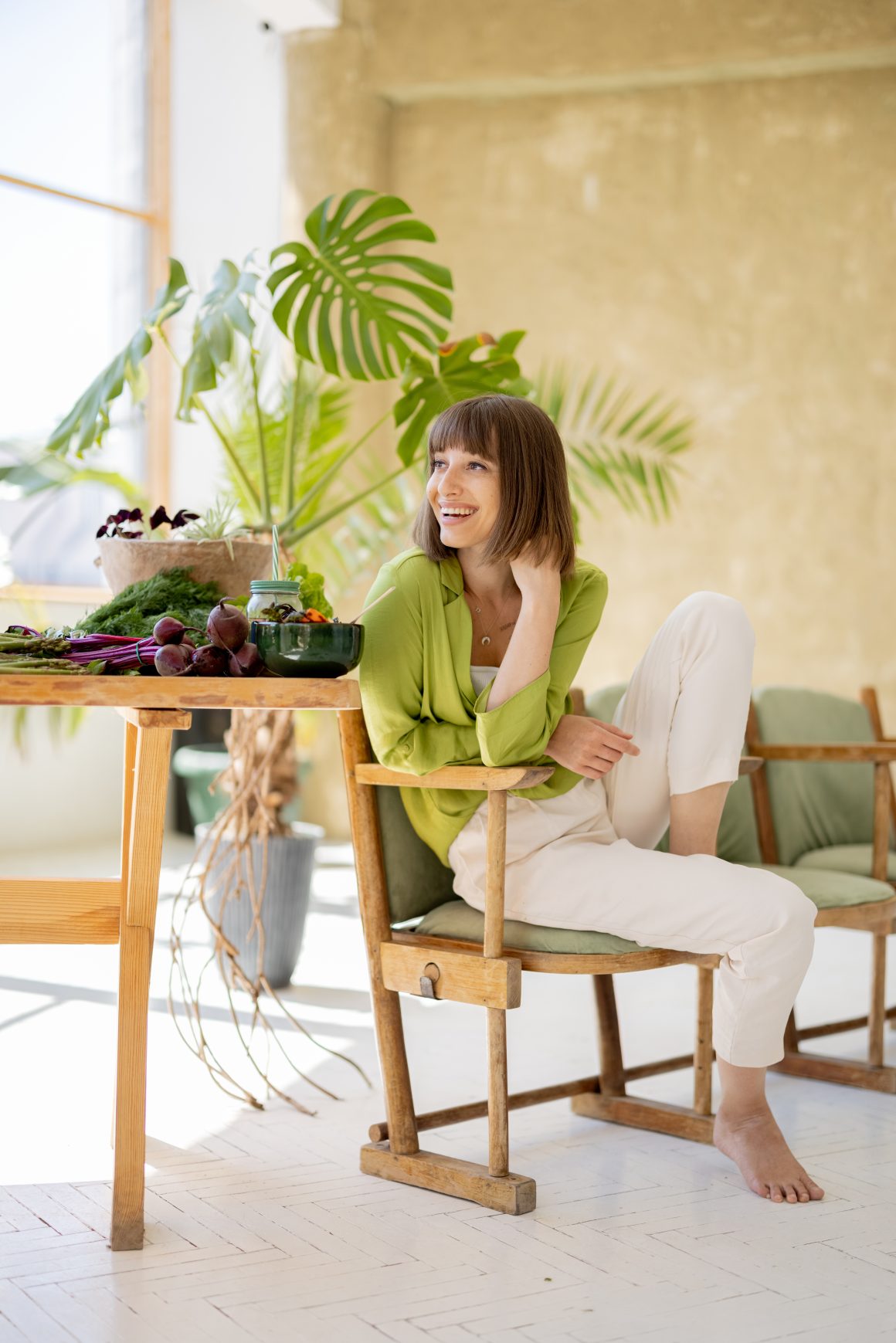 Femme assise sur une chaise en bois clair dans un intérieur maison écologique qui inclut une table en bois et des plantes.