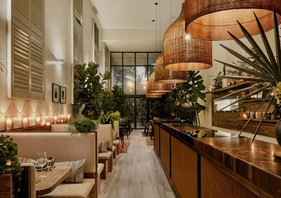 Décoration restaurant avec lumière tamisée, bois naturel, suspensions en osier, plantes vertes et bougies.