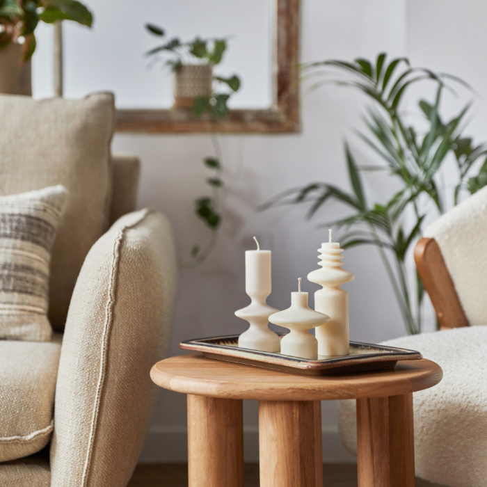 Salon scandinave chaleureux avec bougies, canapé beige, table en bois et plantes.