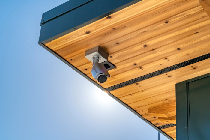 Caméra de surveillance fixée sous un toit en bois clair.
