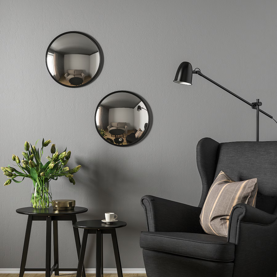 Canapé gris, lampadaire, coussin rayé, tables noires, vase avec fleurs et miroirs ronds.