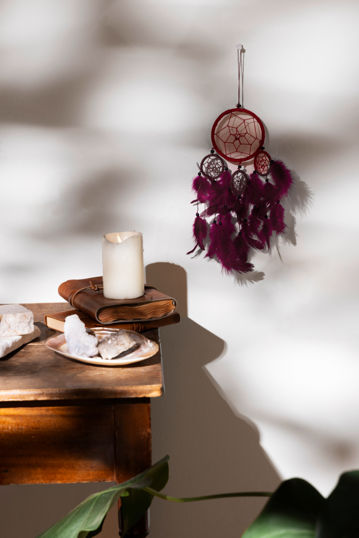 Décor intérieur avec pendentif capteur de rêves, bougie, livres et table en bois.