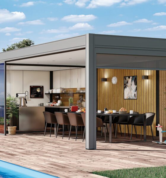 Pool house avec cuisine d'été incluant une grande table à manger noire, des chaises assorties, un bardage bois, une pergola grise, des plantes décoratives, un jouet enfant et un parquet en bois.