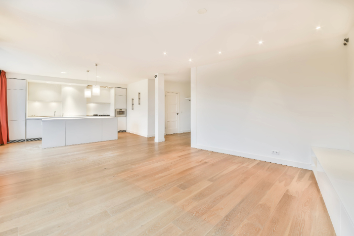 Maison neuve incluant un grand espace ouvert lumineux, sol en bois clair, cuisine moderne blanche avec des murs blancs.