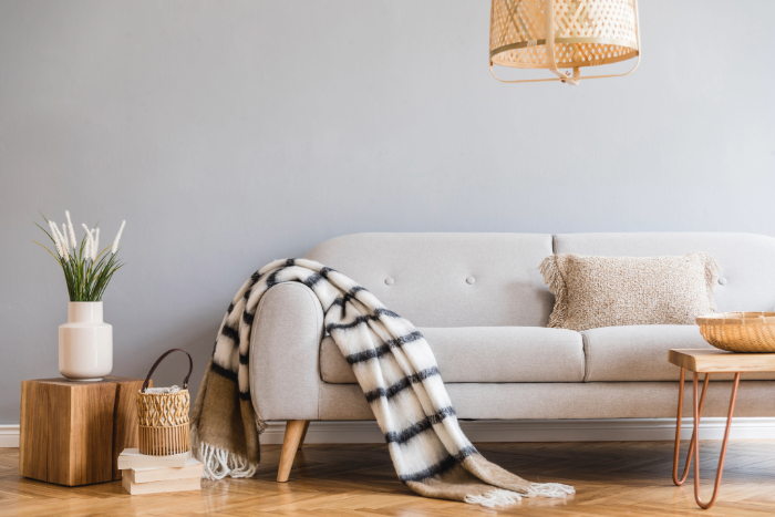 Salon scandinave cocooning avec canapé gris clair, couverture à carreaux, coussin, vase et table en bois.