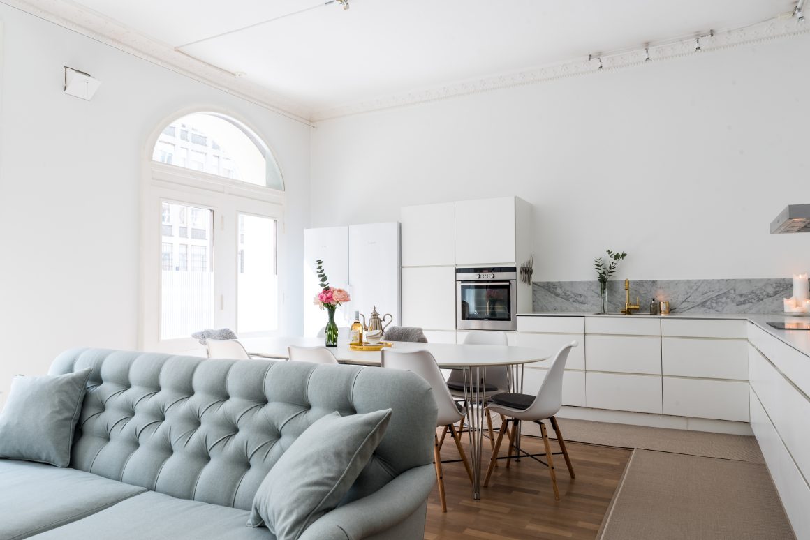 Espace ouvert avec cuisine blanche moderne, table à manger et salon avec canapé gris.