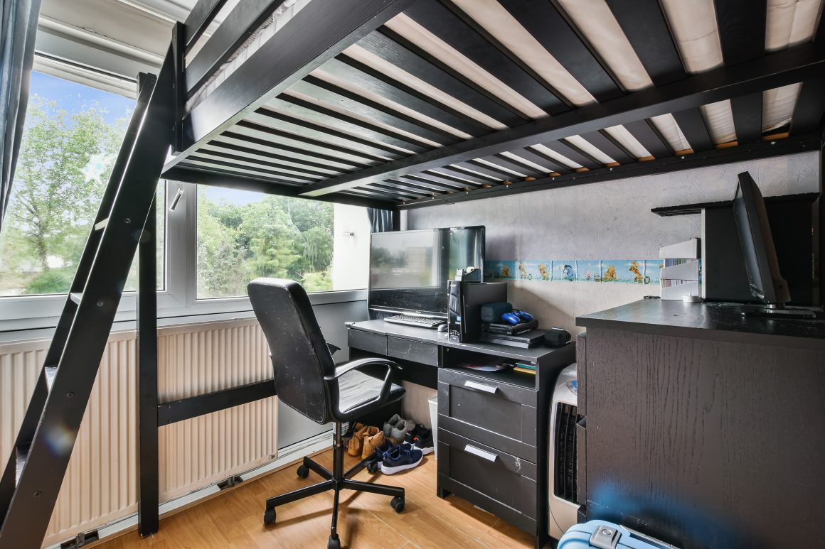 Petit espace de travail sous lit mezzanine avec bureau noir et chaise de bureau.