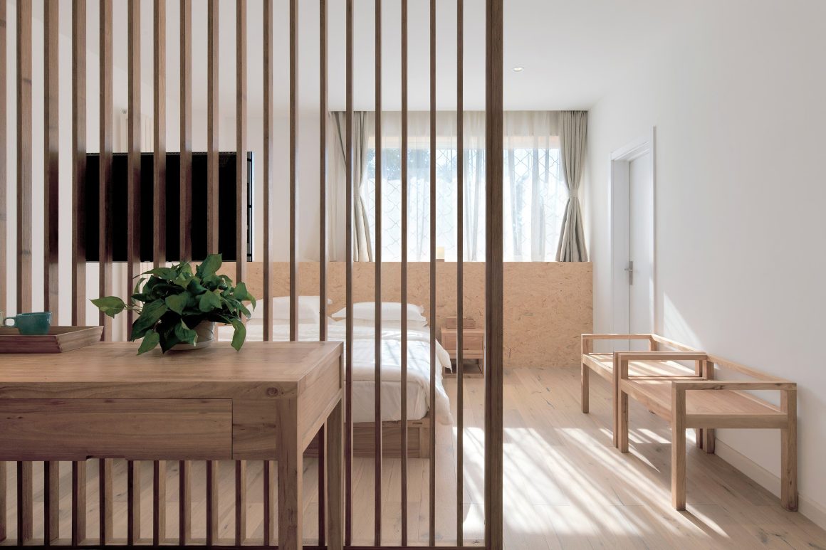 Chambre minimaliste en bois clair, avec séparation verticale, lit, lumière naturelle et plantes.