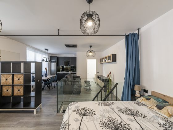 Studio moderne incluant lit, séparation vitrée, coin salon, cuisine équipée et éclairage élégant.