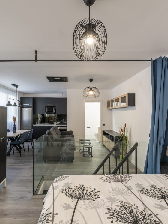 Studio moderne incluant lit, séparation vitrée, coin salon, cuisine équipée et éclairage élégant.