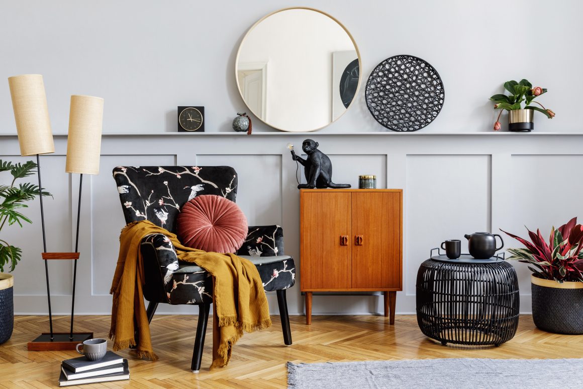 Coin salon avec fauteuil fleuri, miroir rond, lampadaires, plantes et objets de déco tendance 2025.