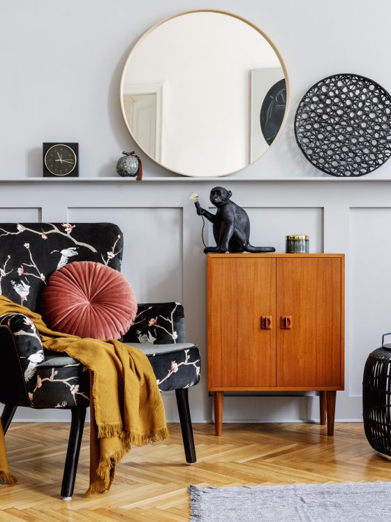 Coin salon avec fauteuil fleuri, miroir rond, lampadaires, plantes et objets de déco tendance 2025.