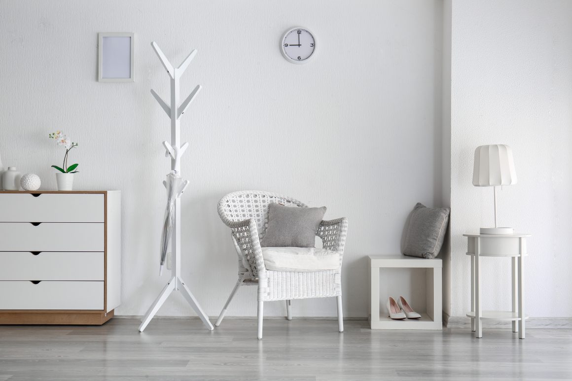 Pièce minimaliste avec mobilier simple : commode, portemanteau, fauteuil et lampe.