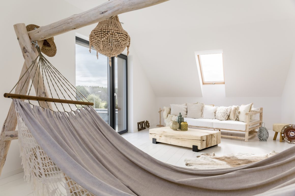 Hamac intérieur dans un salon lumineux avec canapé en bois clair, coussins, table et tapis.