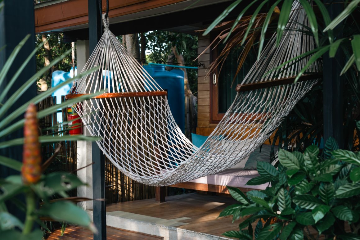 Hamac suspendu en filet blanc sur terrasse bois, entouré de plantes vertes.