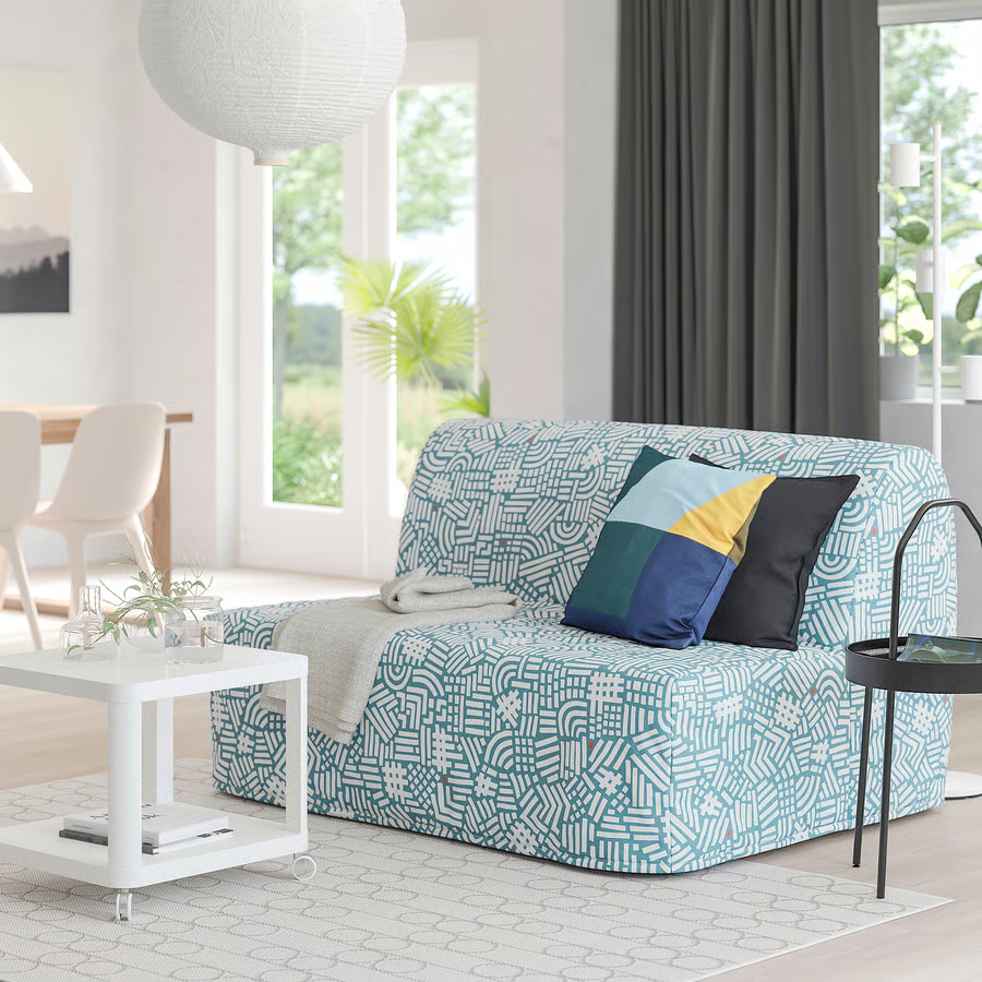 Salon avec canapé géométrique, coussins colorés, tapis beige et grande fenêtre.