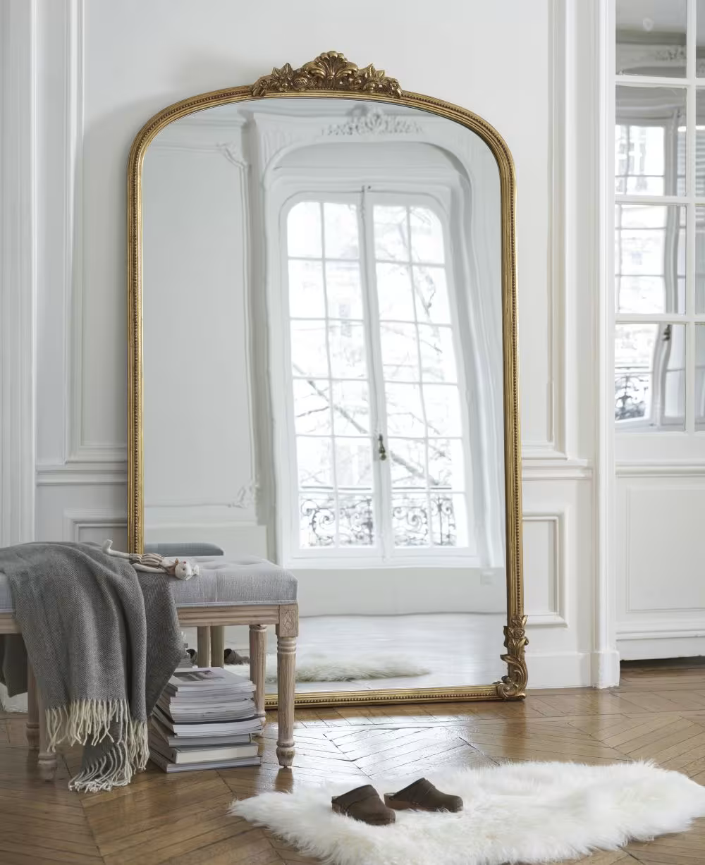 Miroir doré, banc gris avec tapis blanc dans un espace lumineux.