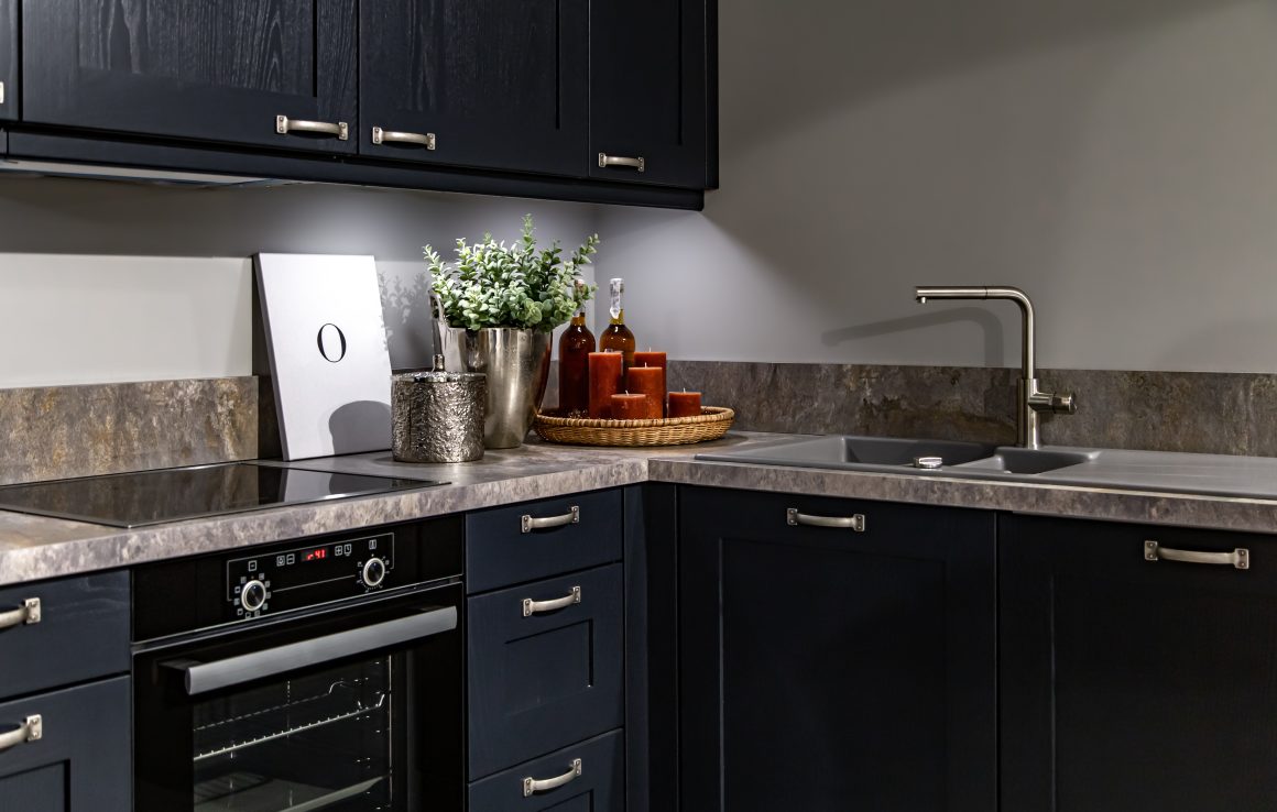 Style de cuisine moderne avec armoires noires, plan de travail en pierre et évier inox.