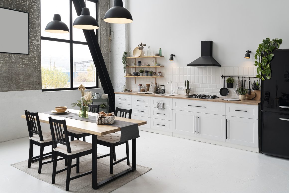 Cuisine blanche avec mobilier noir, grande table en bois, éclairage noir et déco minimaliste.