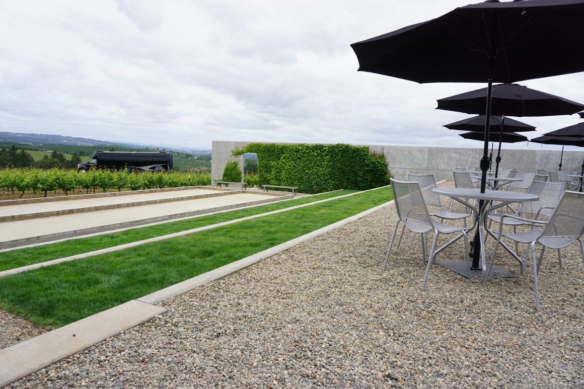 Terrasse avec sol en gravier gris, bordures en béton, et des zones herbeuses.