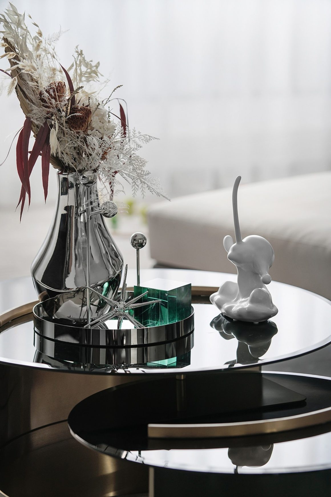 Vase avec fleurs séchées, objet en verre, statuette et décoration moderne sur table noire brillante.