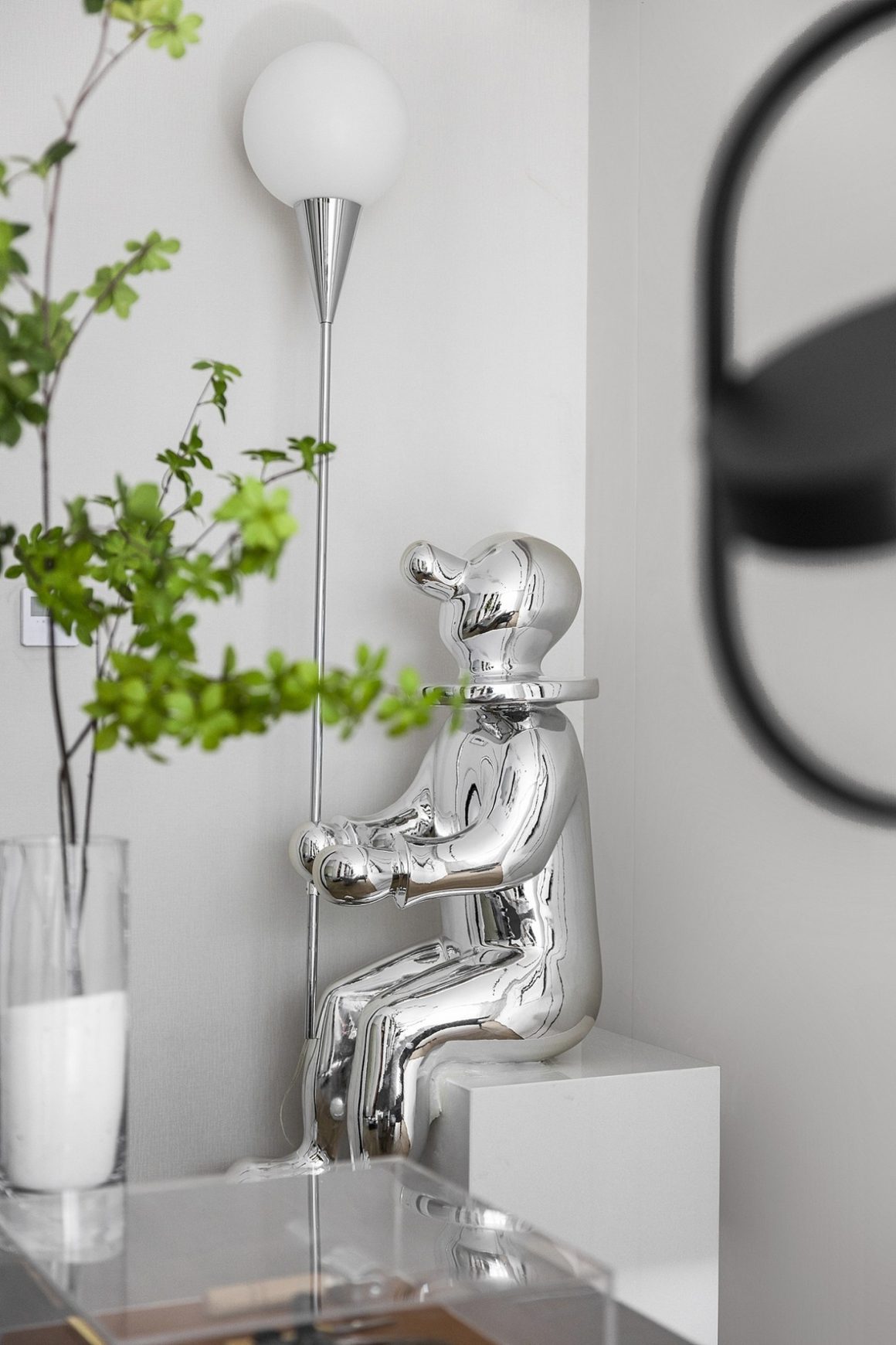 Statue métallique avec lampe en forme de boule blanche et décor végétal.