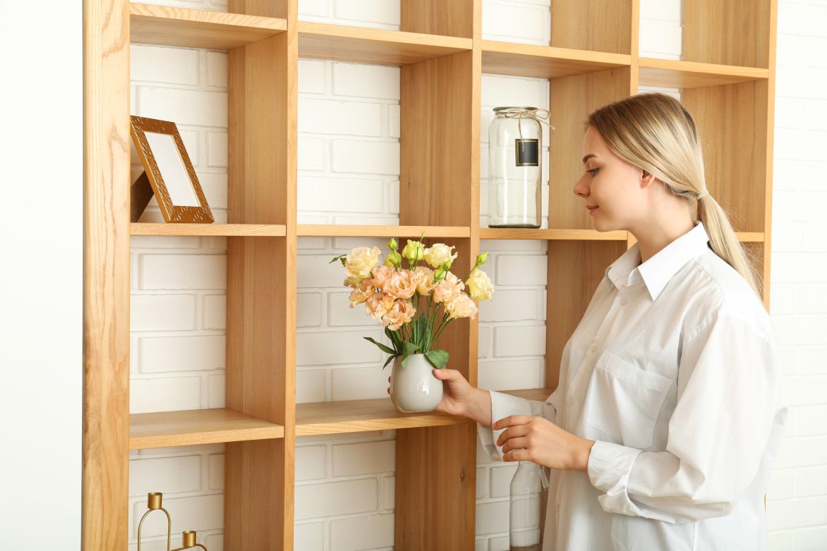 Femme arrangeant fleurs dans une bibliothèque en bois.