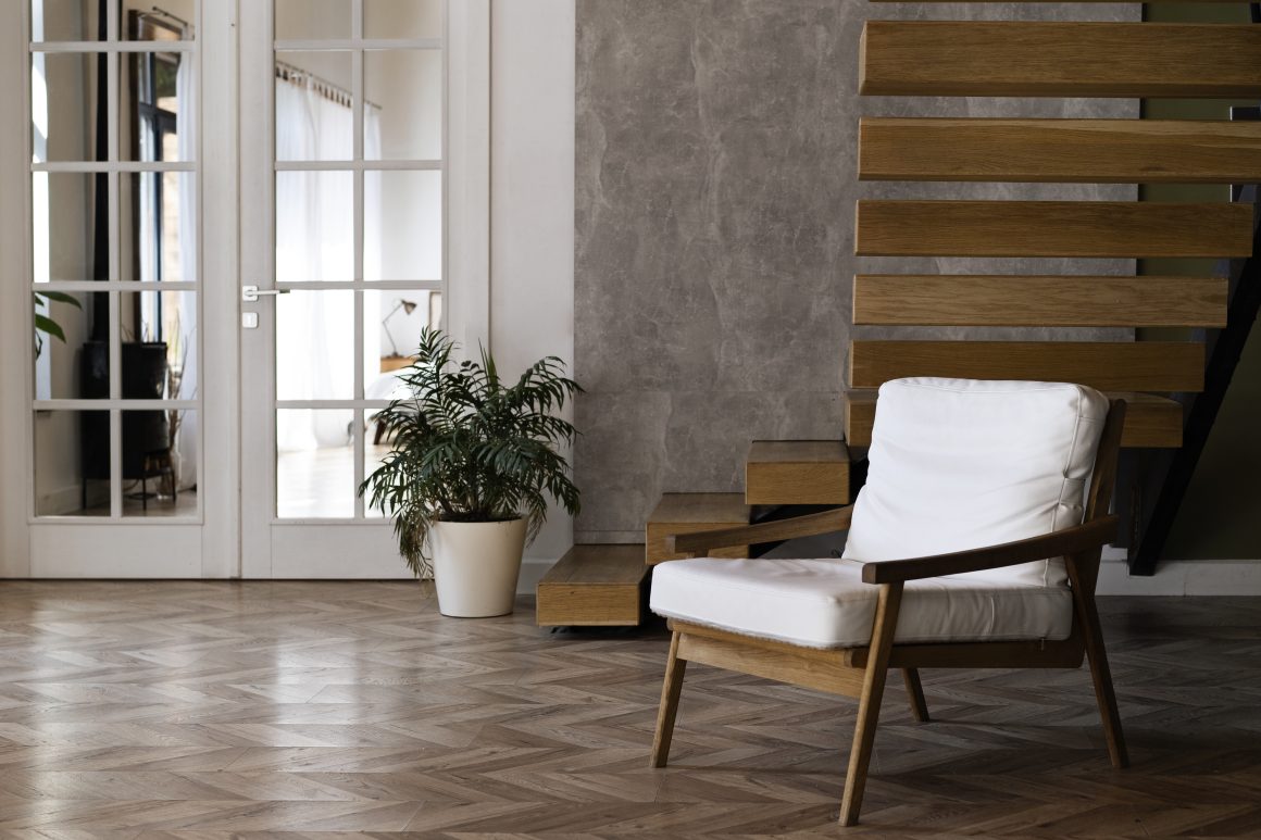 Intérieur moderne avec sol parquet, chaise en bois, escalier , grande porte vitrée et plante.