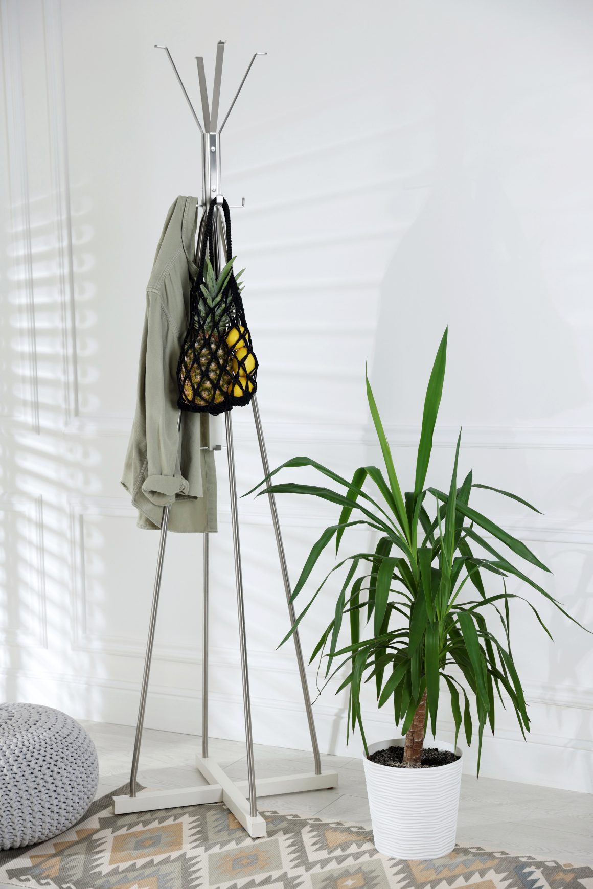 Un portemanteau en métal avec un vêtement et un sac et une plante verte dans un intérieur simple.