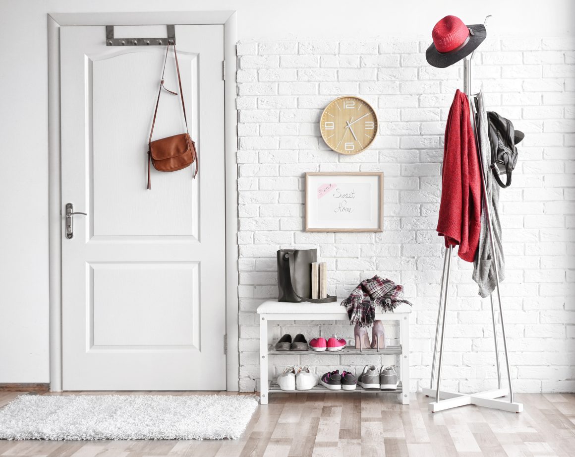 Une entrée épurée avec tapis, portemanteau, étagère à chaussures et décoration murale simple.