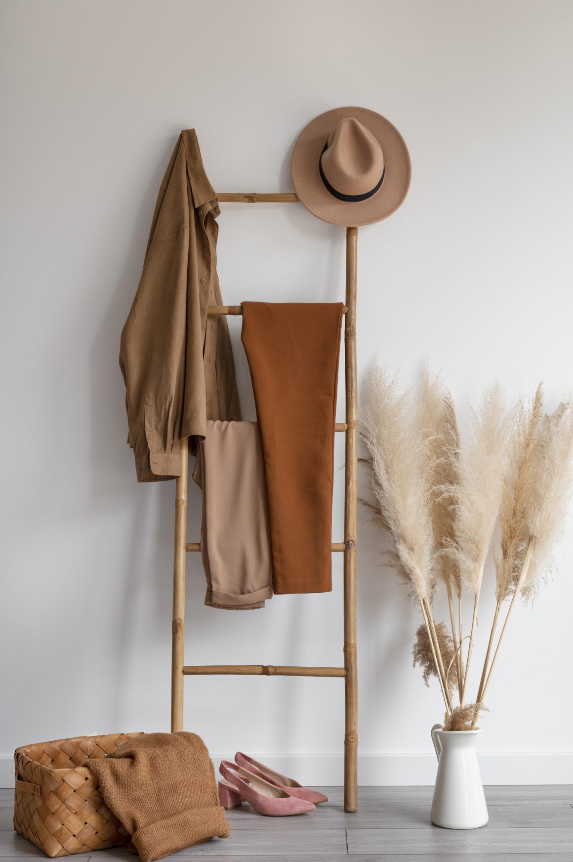 Étagère bambou incluant vêtements, chaussures, et chapeau avec vase pampas et panier.