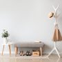 Entrée épurée avec portemanteau blanc, banc gris, table blanche, plante, chaussures et boîte en bois.