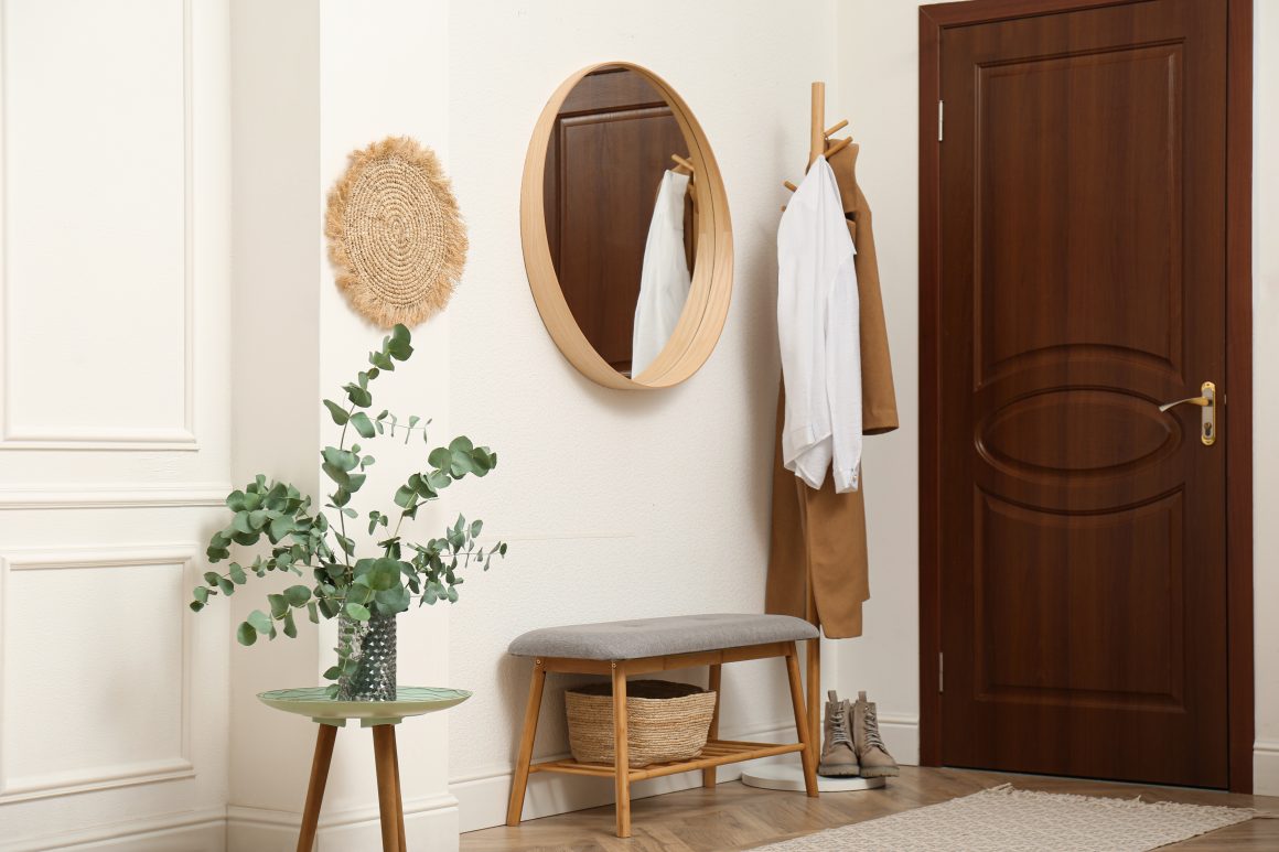 Entrée avec porte-manteau en bois, miroir, banc, panier et plante.