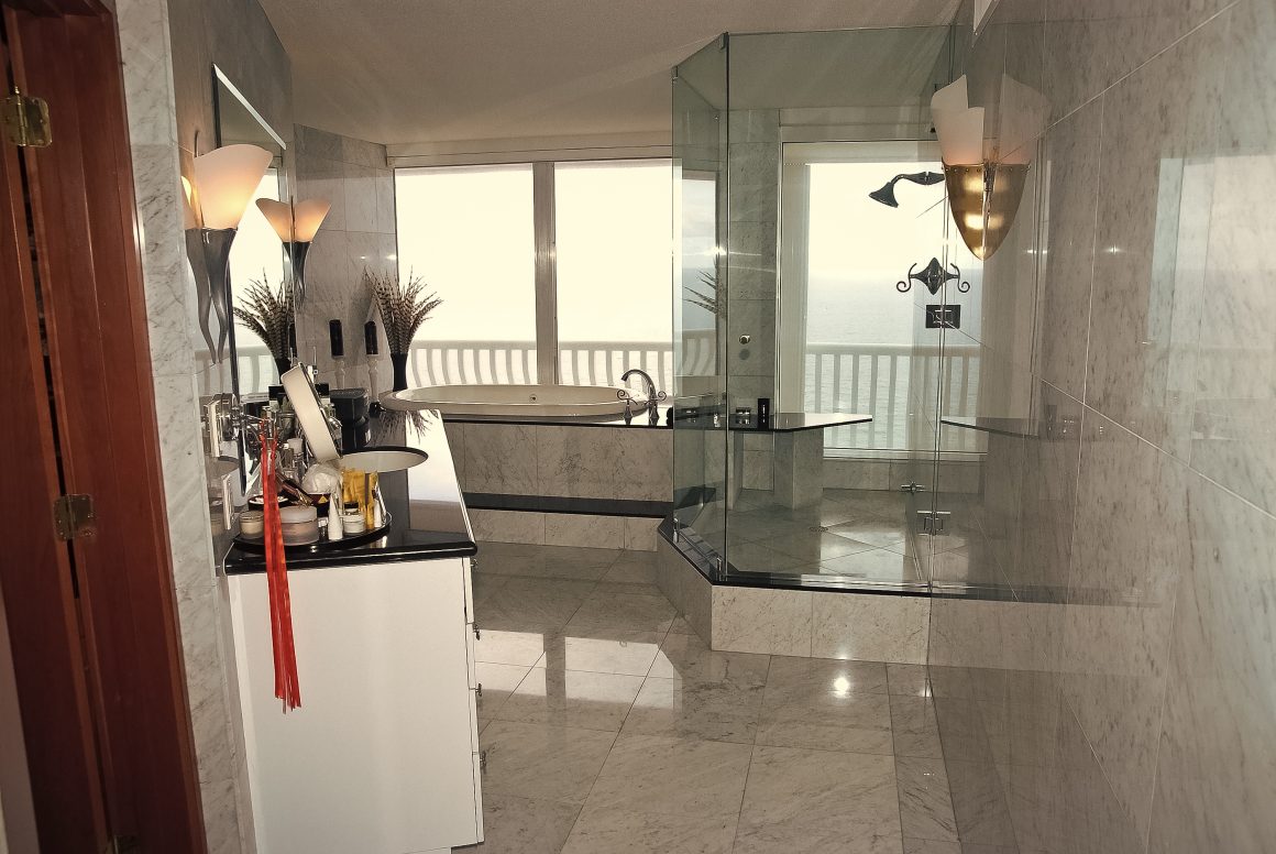 Salle de bain élégante avec carrelage en grès cérame clair, grande douche en verre et baignoire spacieuse.