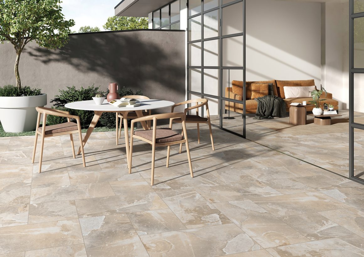 Terrasse avec sol tendance 2025 en carrelage beige, table, chaises en bois, canapé, plantes et grande baie vitrée.