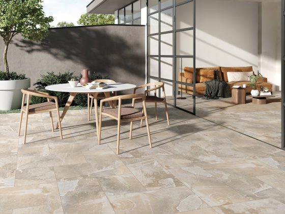 Terrasse avec sol tendance 2025 en carrelage beige, table, chaises en bois, canapé, plantes et grande baie vitrée.
