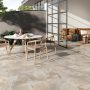 Terrasse avec sol tendance 2025 en carrelage beige, table, chaises en bois, canapé, plantes et grande baie vitrée.