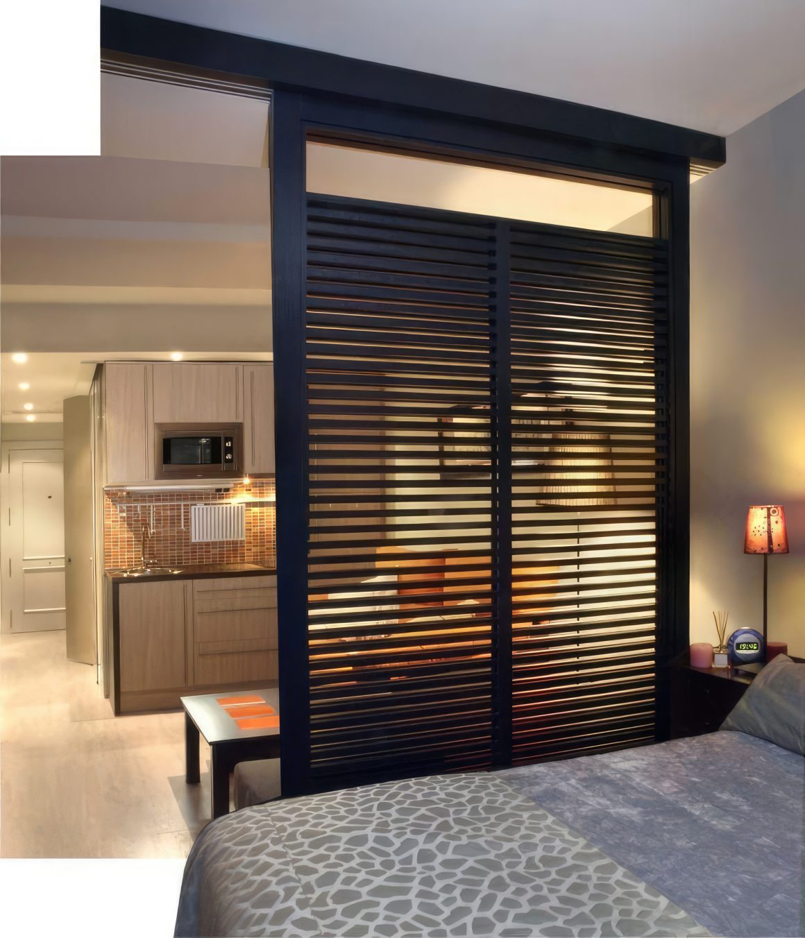 Chambre avec lit, lampe et séparation en lattes noires.