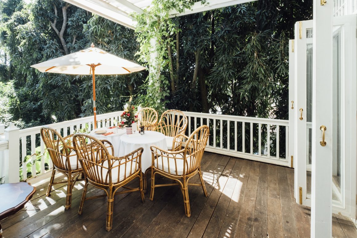 Balcon avec table ronde, chaises en rotin, parasol, plantes et sol en bois.