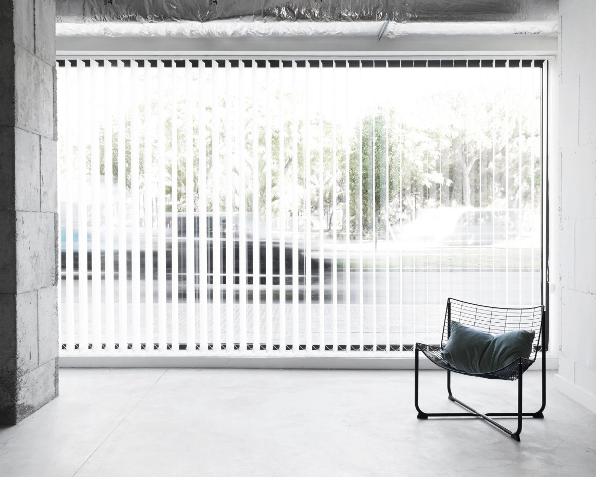 Espace minimaliste avec fauteuil noir et baie vitrée avec stores blancs.