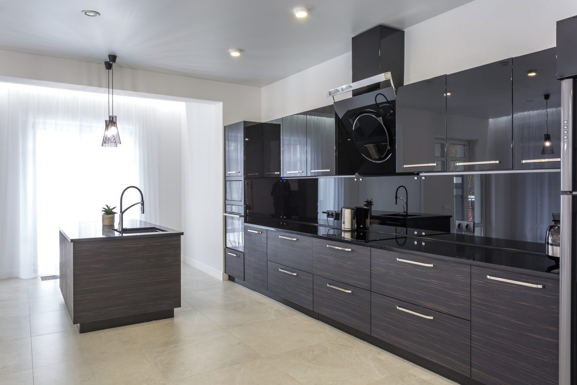 Cuisine moderne équipée incluant meubles noirs brillants, îlot central avec évier et appareils inoxydables.